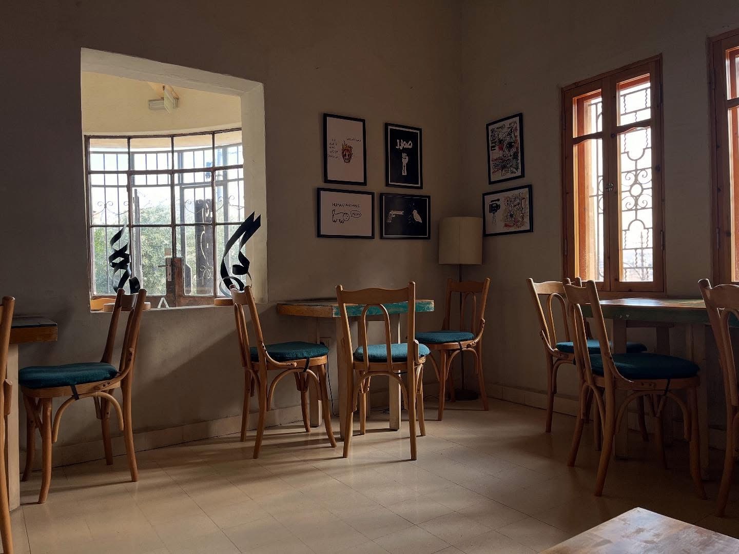 Quiet interior room at Fann wa Chai with bentwood chairs, teal cushions, Arabic calligraphy sculptures in the window, and framed illustrations on the wall