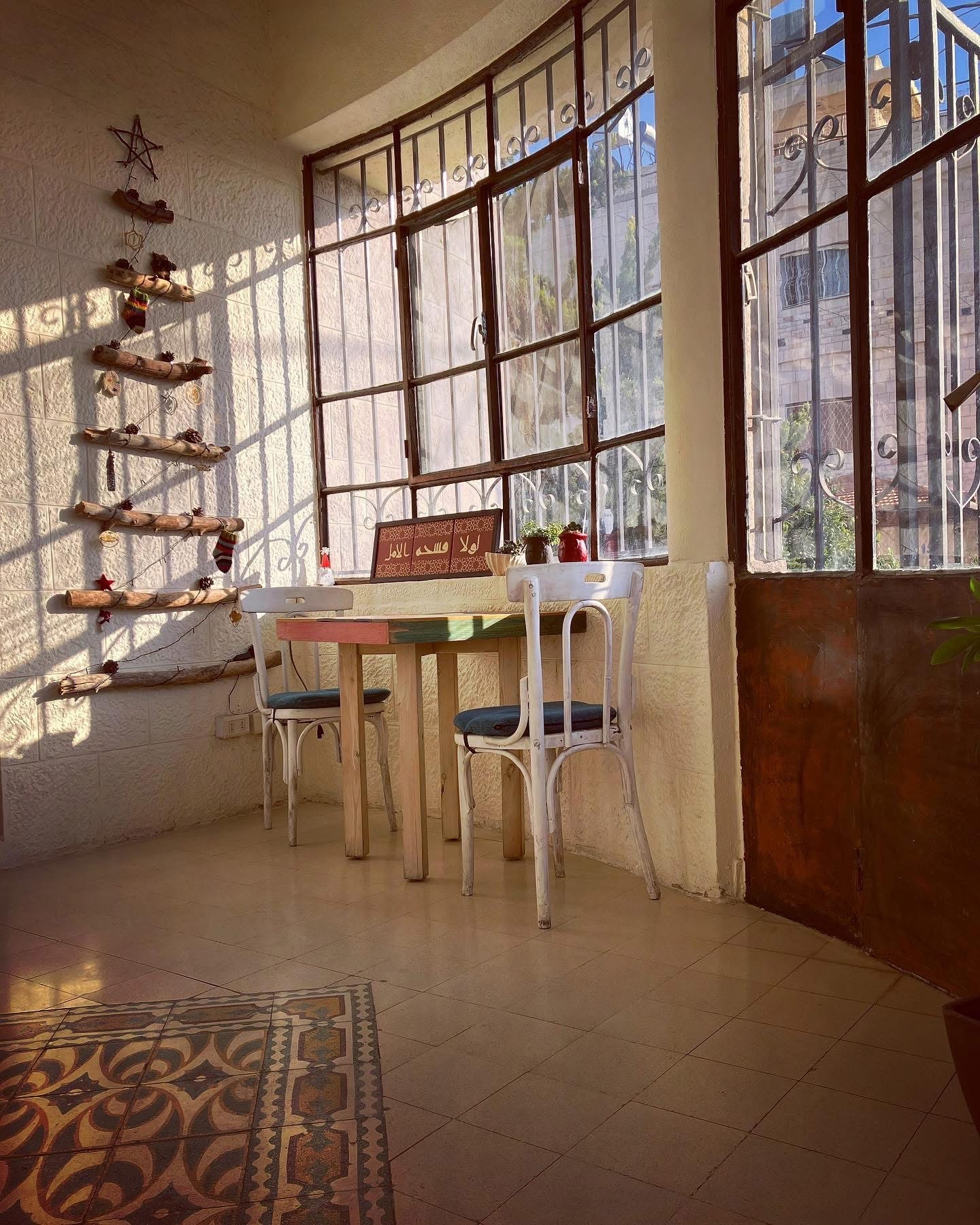 A bright sunroom corner at Fann wa Chai with a driftwood wall ornament, patterned tile floor, and a small painted table for two by curved windows