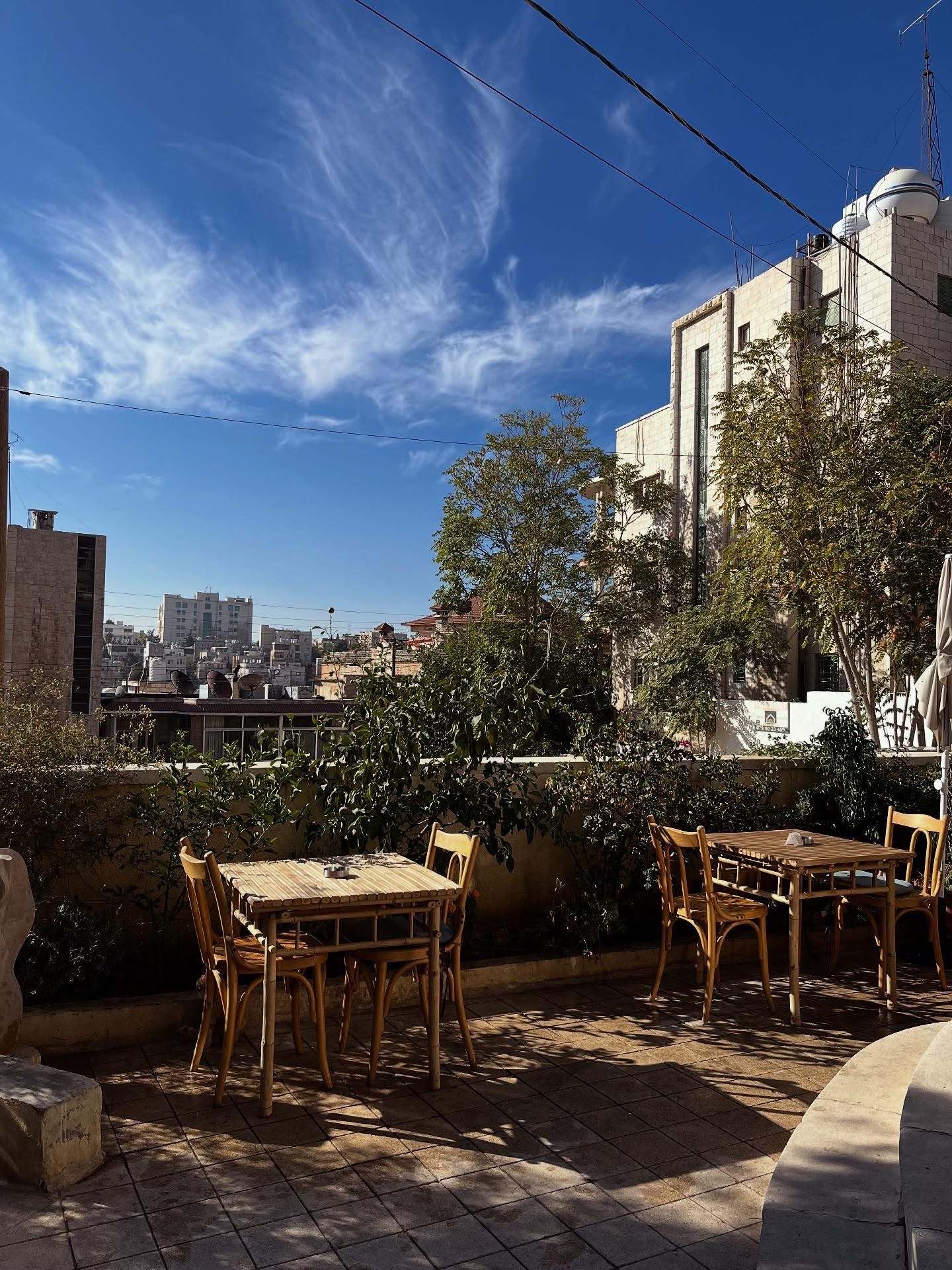 Bamboo tables on the sunny terrace of Fann wa Chai under a bright blue sky, looking out over the rooftops of Amman